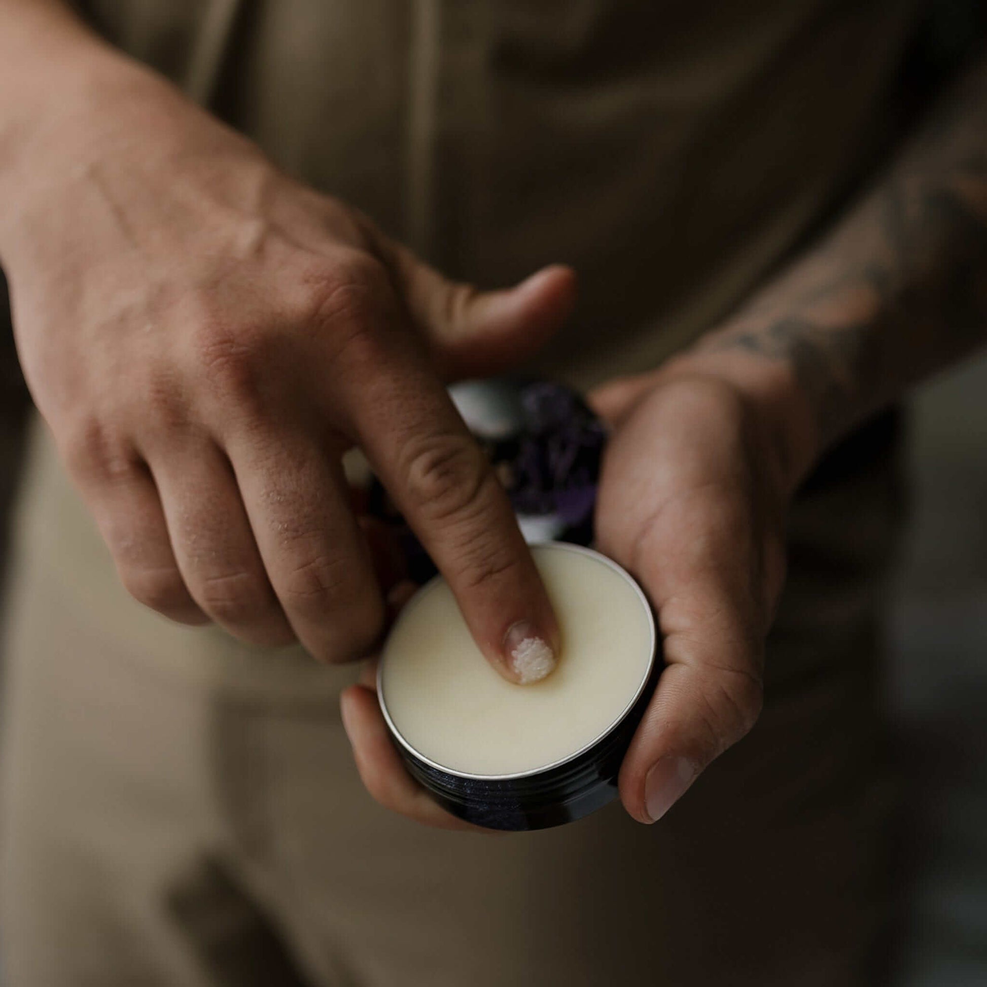 Man scraping natural beard balm from tin with finger – Warlord natural beard balm application, masculine men’s grooming, rugged hands-on routine.