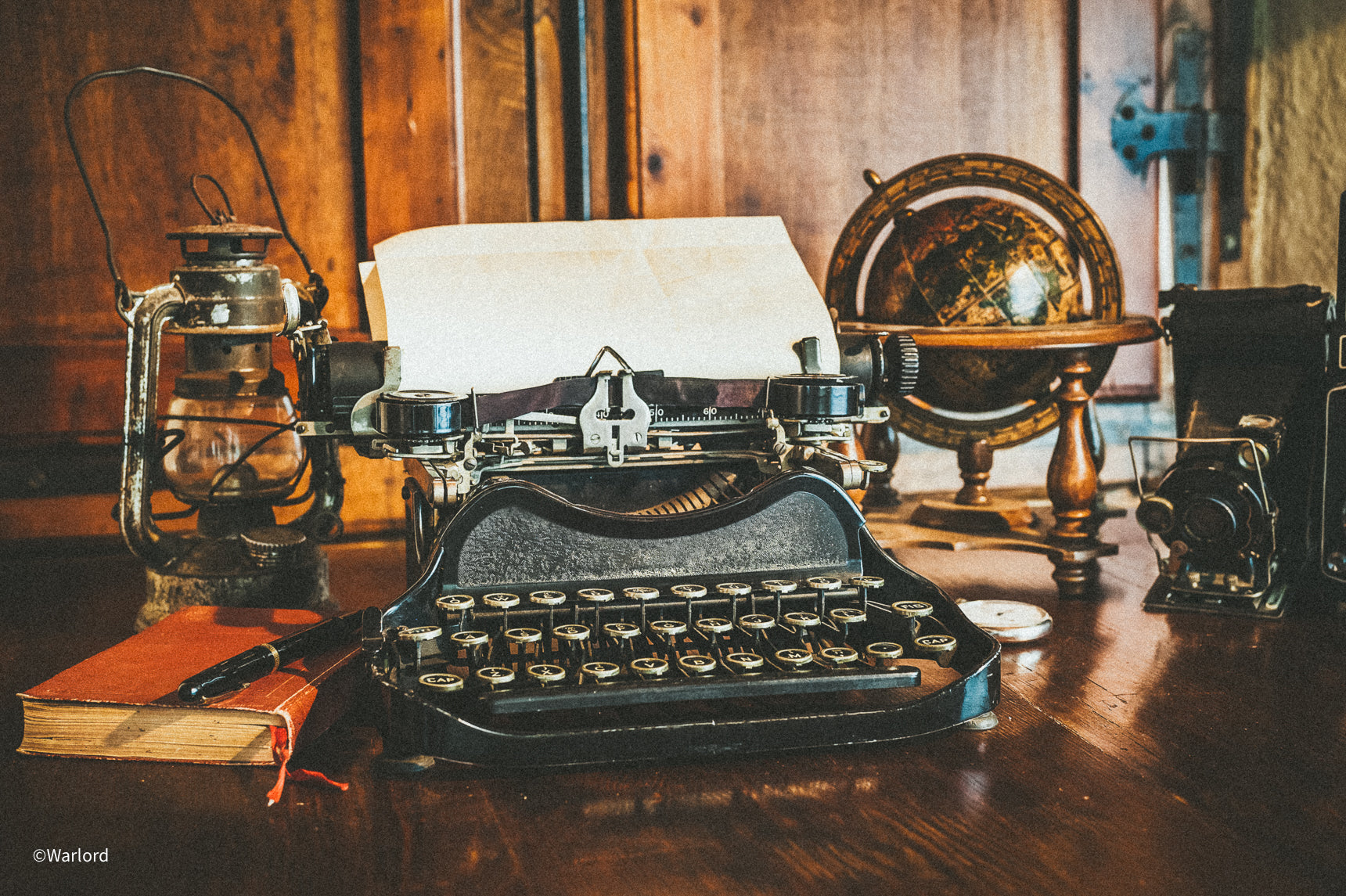 Vintage typewriter with paper, paired with an old-fashioned oil lamp, a book, and a pen, all set on a mahogany desk in a stately office. A classic globe and vintage camera add to the scene's ambiance - Timeless elegance and intellectual charm with Warlord Grooming sophistication.