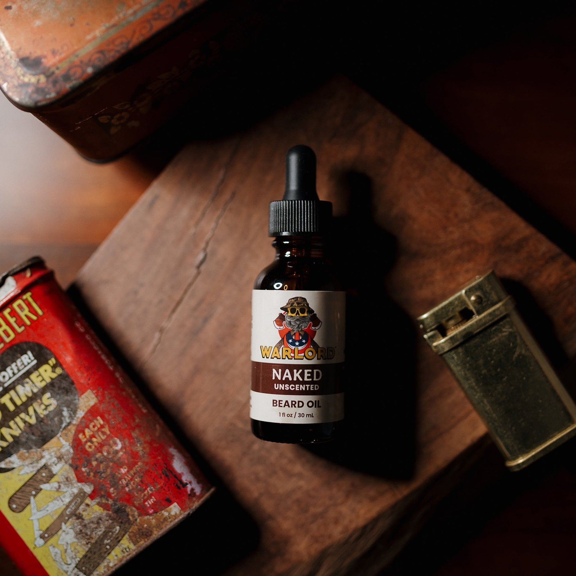 Warlord Naked Unscented Beard Oil bottle on a rustic wood surface, styled with a vintage lighter and red Prince Albert tin for a rugged, old-school vibe.